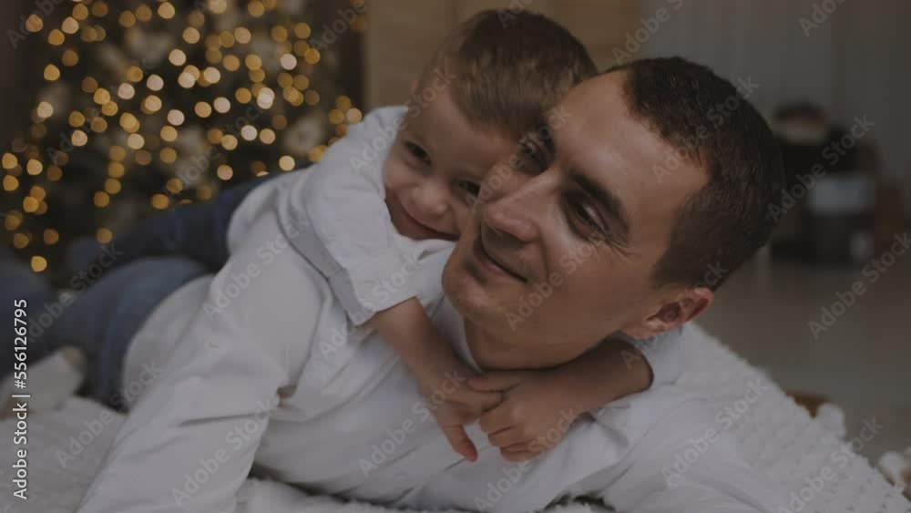 Little son smiling and hugging his father lying on the bed against the background of the Christmas tree.