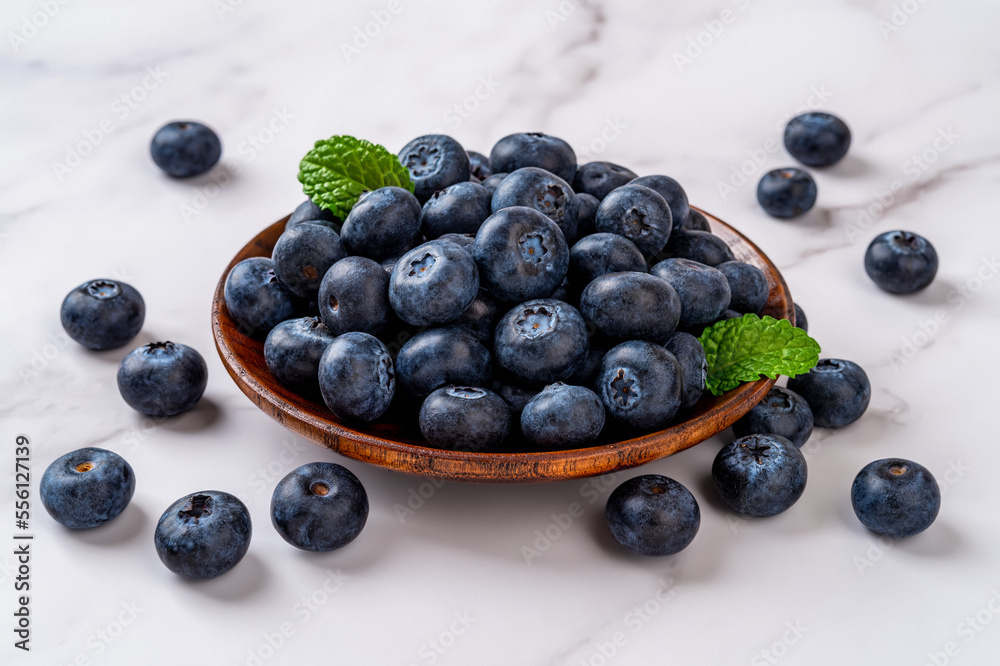 Ripe blueberry on a wooden plate over marble background. Fresh sweet blueberries for vitamin vegan snack. Wild berry as natural antioxidant for healthy eating. Vegetarian dessert. Ripe blueberry on a wooden plate over marble background. Fresh sweet blueberries for vitamin vegan snack. Wild berry as natural antioxidant for healthy eating. Vegetarian dessert.