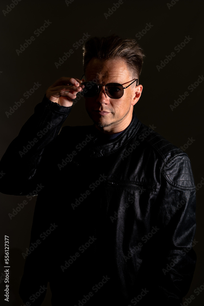 Portrait of handsome male. Sexy stylish man dressed in a leather jacket and sunglasses. Fashion hipster male isolated on grey background in studio Portrait of handsome male. Sexy stylish man dressed in a leather jacket and sunglasses. Fashion hipster male isolated on grey background in studio