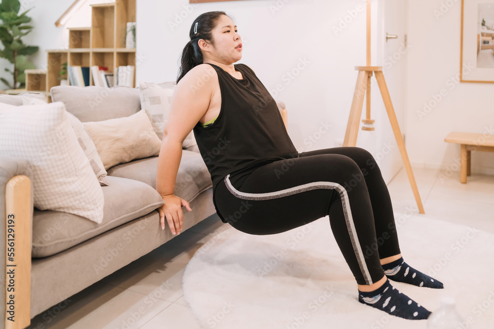 fat woman doing sofa exercise indoors living room tricep dip. motivated