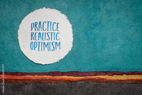 practice realistic optimism - inspirational advice or reminder, writing against abstract paper landscape, positivity concept photo