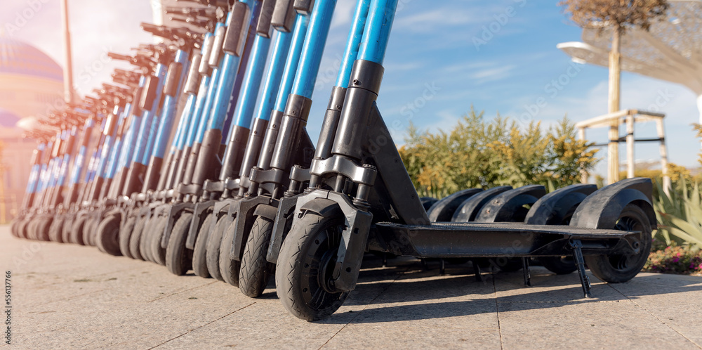 Row rent electric scooters parked on city street rental service with sunlight. Concept banner eco energy transport