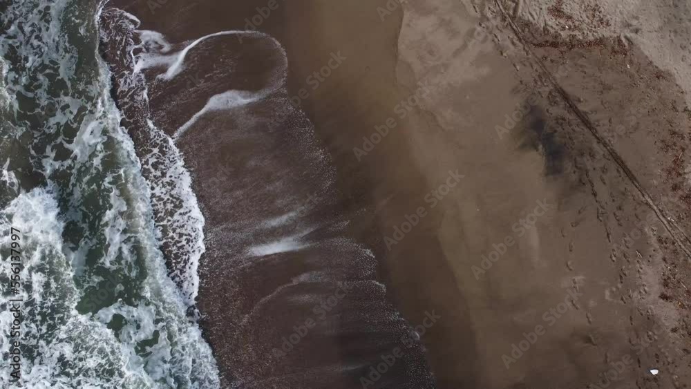 Drone shot of foamy sea waves crashing on the gold colored shoreline, rough sea with waves and wind. rocks