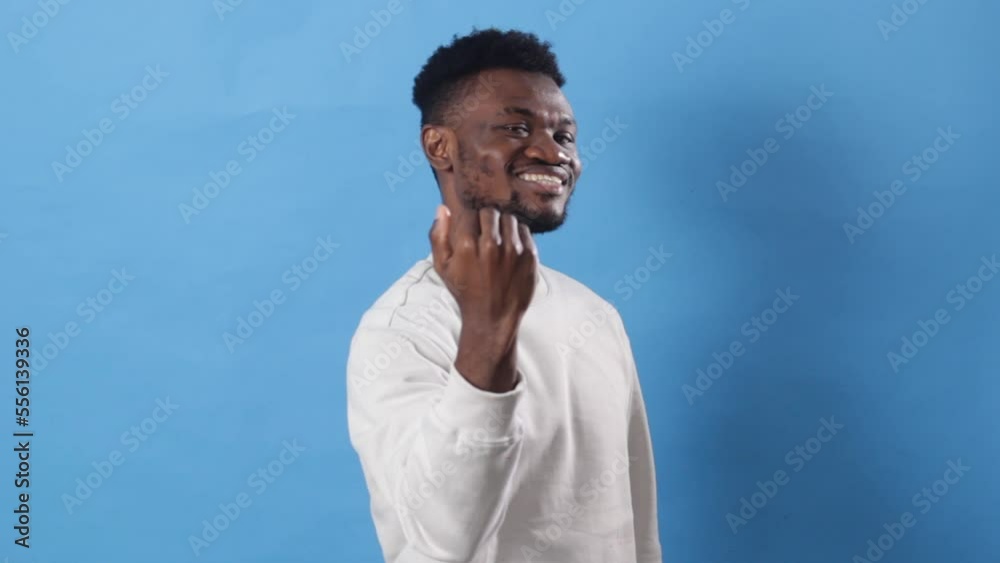 A young African man with, standing on a blue background, beckoning to come here with a hand gesture, inviting, greeting, happy and smiling. A young African man with, standing on a blue background, beckoning to come here with a hand gesture, inviting, greeting, happy and smiling.
