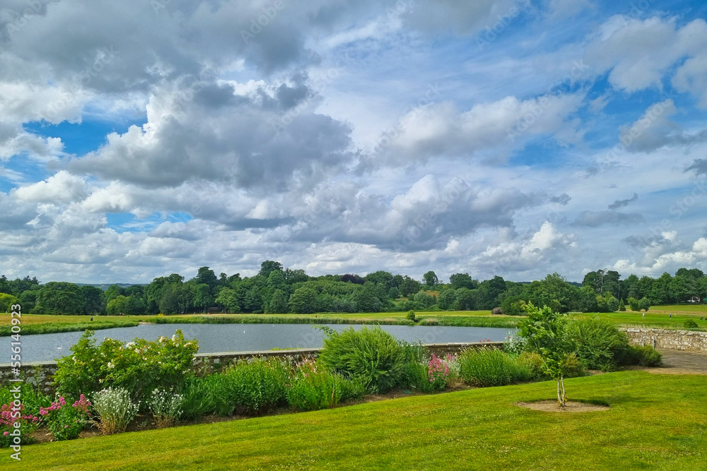 Beautiful view of the lake and the green meadow in the park. A sunny summer day with large white clouds in the sky.