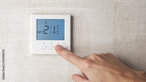 male hand turning up the temperature from 19 to 22 degrees on a digital thermostat photo