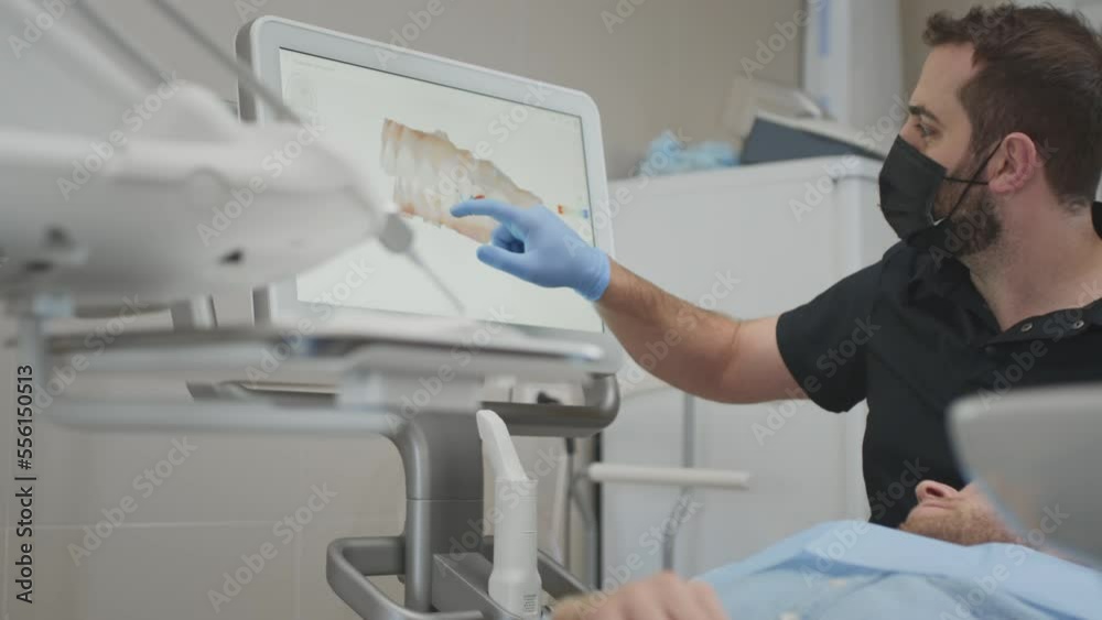 A male orthodontist doctor shows on the display a 3d model of the oral cavity of a man patient. Medical examination of teeth. Digital scanning with a scanner, checking the jaw. Dental clinic office. A male orthodontist doctor shows on the display a 3d model of the oral cavity of a man patient. Medical examination of teeth. Digital scanning with a scanner, checking the jaw. Dental clinic office.