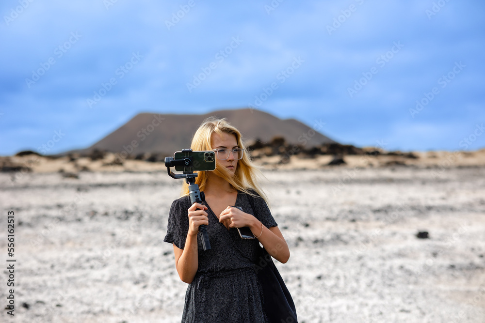 Obraz premium A blogger girl visits the famous Popcorn Beach in Fuerteventura. A young traveler uses her mobile phone outdoors. Travel and freelancing, modern lifestyle concept.