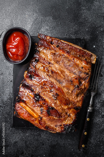 Full rack of BBQ grilled pork spare ribs on a marble board. Black background. Top view