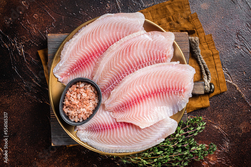 Raw fish fillet of tilapia in a plate with spices. Dark background. Top view photo