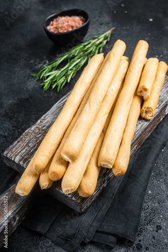 Italian grissini or salted bread sticks on wooden board. Black bakground. Top view