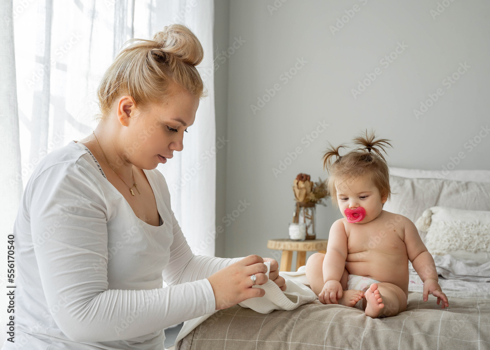 Mother changing clothes or nappy of baby toddler girl on bed at home. Child care, healthy