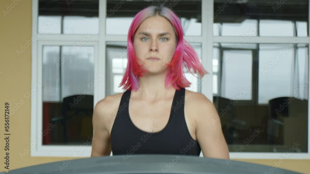 Focused female athlete jogging during intensive workout. Beautiful young woman with pink hair running on a treadmill for a weight loss. High quality 4k footage Focused female athlete jogging during intensive workout. Beautiful young woman with pink hair running on a treadmill for a weight loss. High quality 4k footage