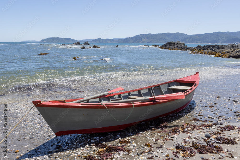 Red and white painted rowing boat at the beach at Isla Maiquillahue in the Pacific Ocean of Chile
