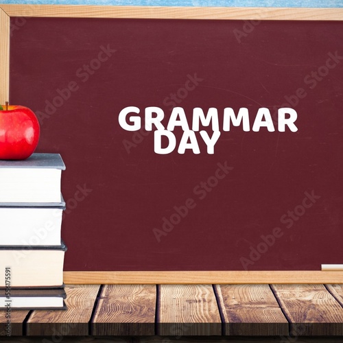 Apple over stack of books on wooden table against grammar day text banner on blackboard