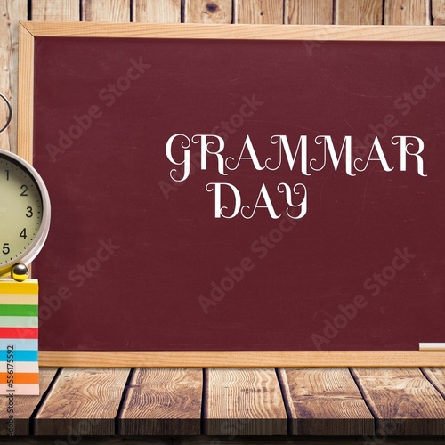 Alarm clock over a wooden table against grammar day text banner on blackboard