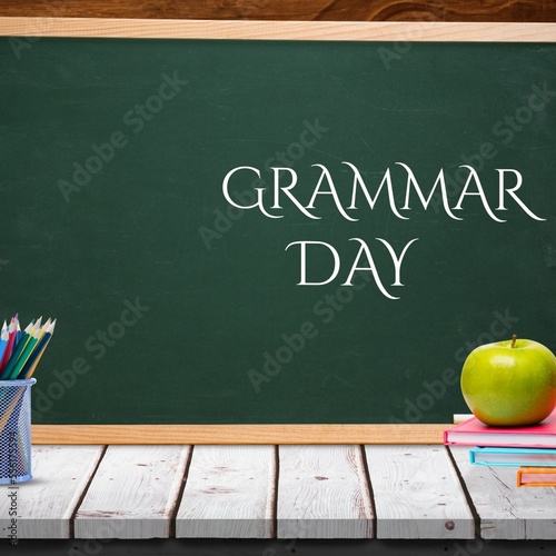 Apple over stack of books on wooden table against grammar day text banner on blackboard