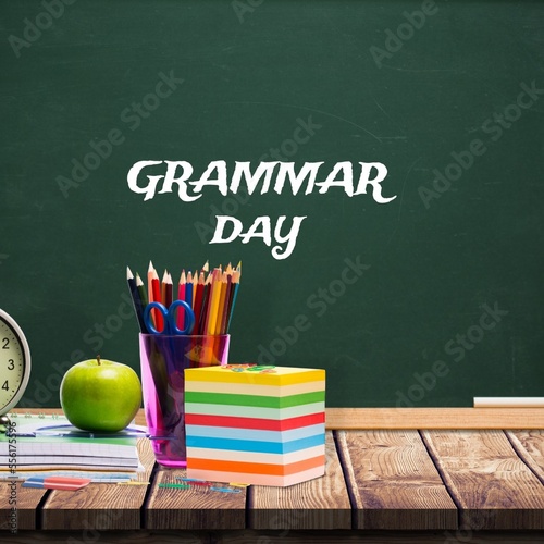 School equipment on wooden table against grammar day text banner on blackboard