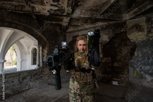 Caucasian woman in army uniform holding two machine guns. 
