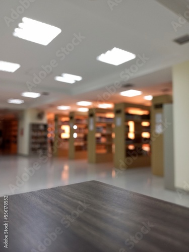 Empty wooden table top with blurred bookshelves as its background.
