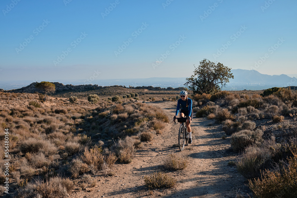 woman cyclist riding a gravel bicycle on the road in hills with mountain view, Alicante region in Spain 