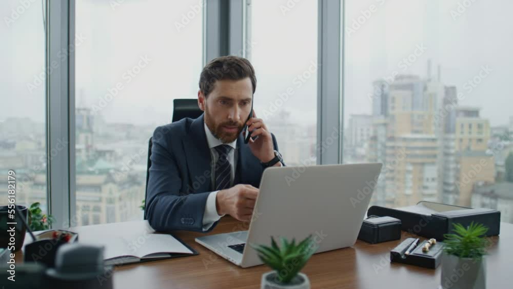 Businessman making business call checking information from laptop on office desk Businessman making business call checking information from laptop on office desk