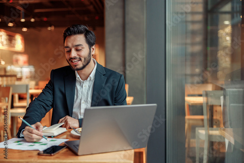 Smiling businessman working with graphs and charts at modern cafe