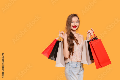 Stylish young woman with shopping bags on orange background, space for text