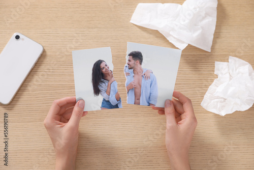 Woman holding torn photo near paper napkins at wooden table, top view. Divorce concept photo