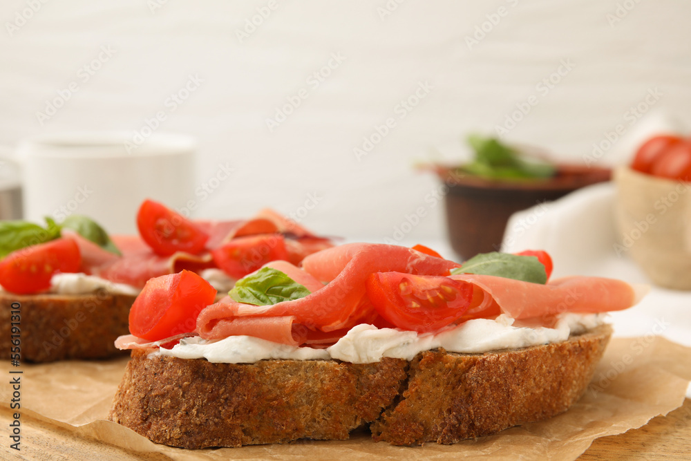 Tasty bruschettas with prosciutto, tomatoes and cheese on wooden board, closeup