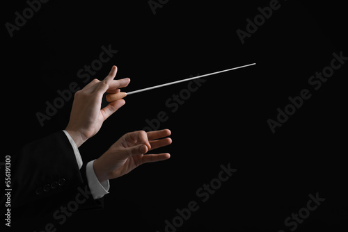 Professional conductor with baton on black background, closeup. Space for text