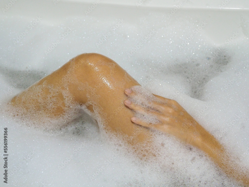 Fototapeta premium Relaxed Asian woman rubbing the skin of her legs with bubbles in the bathtub.