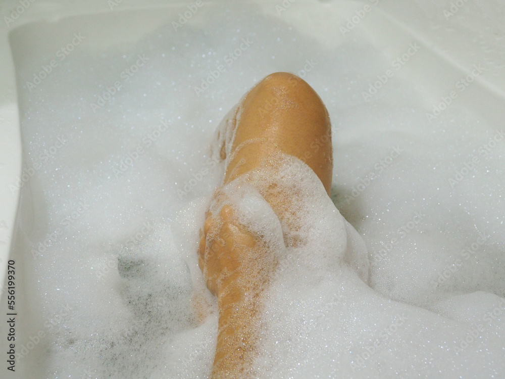 Fototapeta premium Relaxed Asian woman rubbing the skin of her legs with bubbles in the bathtub.