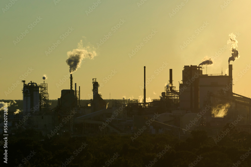Aerial view of large factory with smokestack from production process polluting atmosphere at plant manufacturing yard. Industrial site at sunset