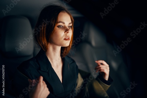 a close horizontal portrait of a stylish, luxurious woman in a leather coat sitting in a black car at night in the passenger seat © SHOTPRIME STUDIO
