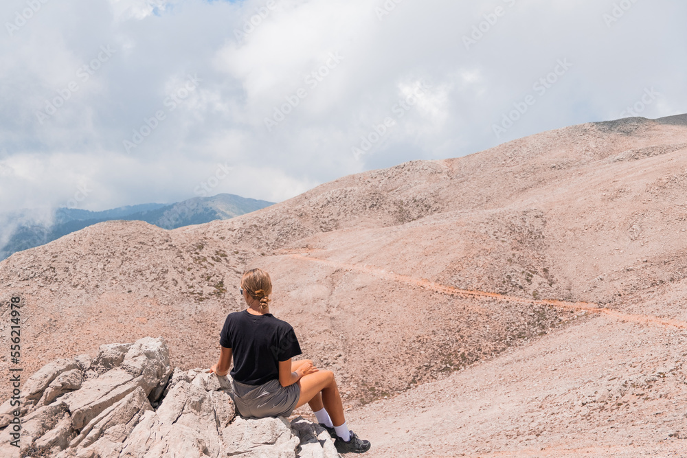The girl is sitting on the edge of a high mountain in the clouds. The girl looks at the beautiful mountain landscape of Antalya, Turkey The girl is sitting on the edge of a high mountain in the clouds. The girl looks at the beautiful mountain landscape of Antalya, Turkey