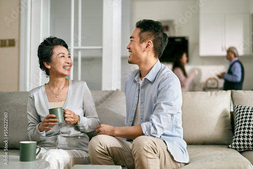 asian elderly mother and visiting adult son chatting at home photo