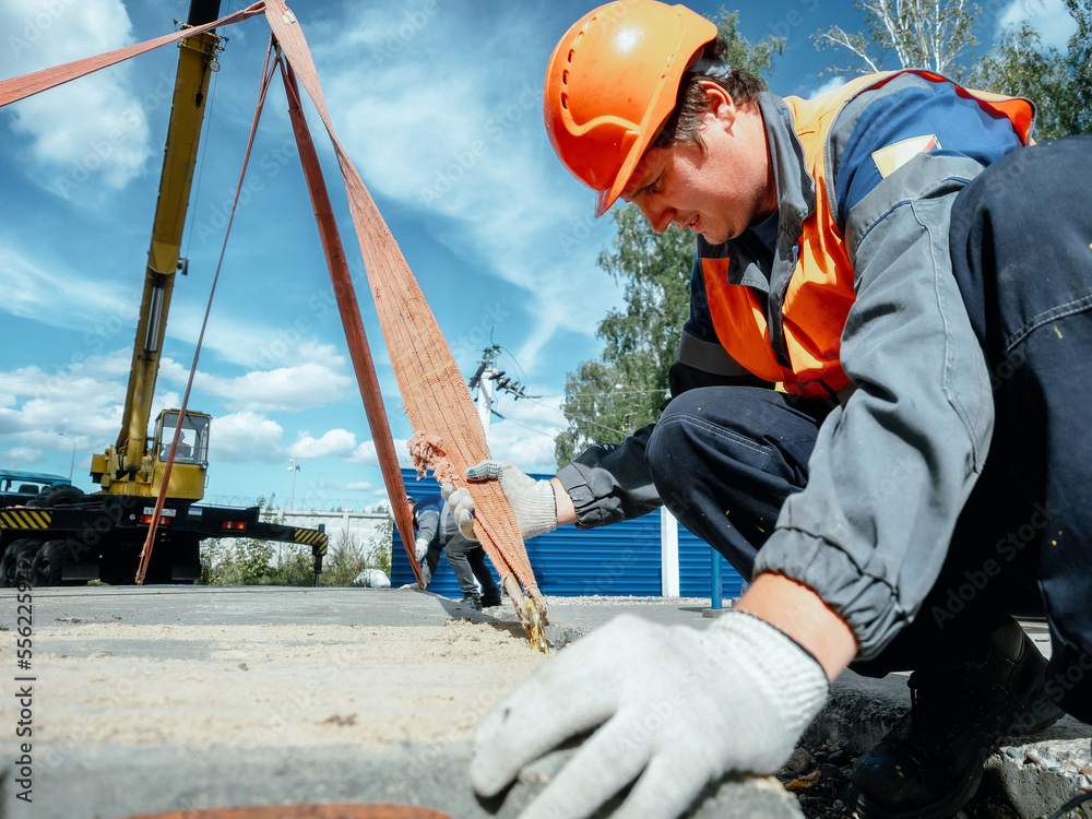 Slinger lays concrete slab on construction site on summer day. Worker