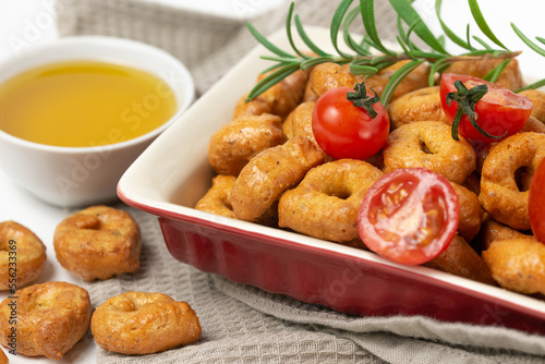 Vegetable taralli or tarallini with rosemary and tomatoes in plate an olive oil in bowl close up