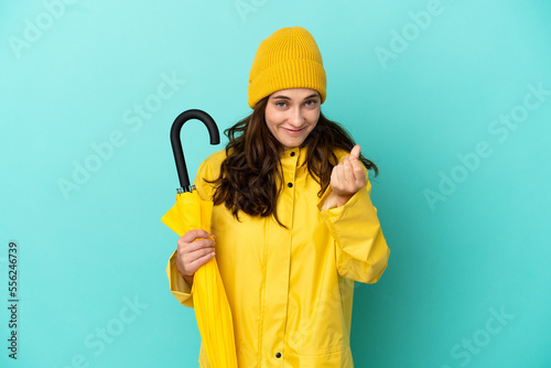 Young caucasian man holding an umbrella isolated on blue background making money gesture