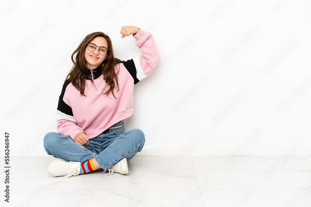 Young caucasian woman sitting on the floor isolated on white background doing strong gesture Young caucasian woman sitting on the floor isolated on white background doing strong gesture