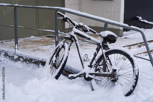 Bicycle under snow near the building entrance, winter in the city
