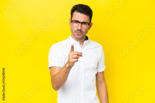 Young handsome man over isolated yellow background frustrated and pointing to the front