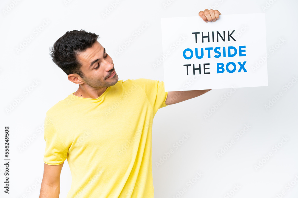 Young handsome man over isolated white background holding a placard with text Think Outside The Box Young handsome man over isolated white background holding a placard with text Think Outside The Box
