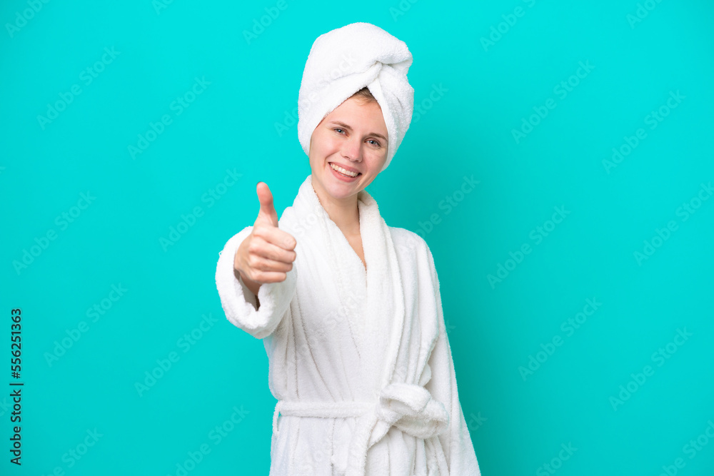 Young woman in a bathrobe isolated on blue background with thumbs up because something good has happened