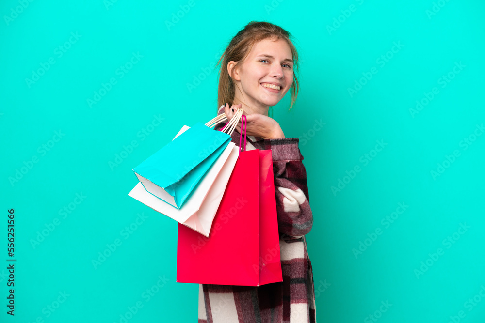 Young English woman isolated on blue background holding shopping bags and smiling