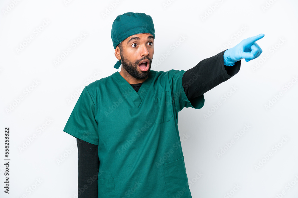 Surgeon Brazilian man in green uniform isolated on white background pointing away