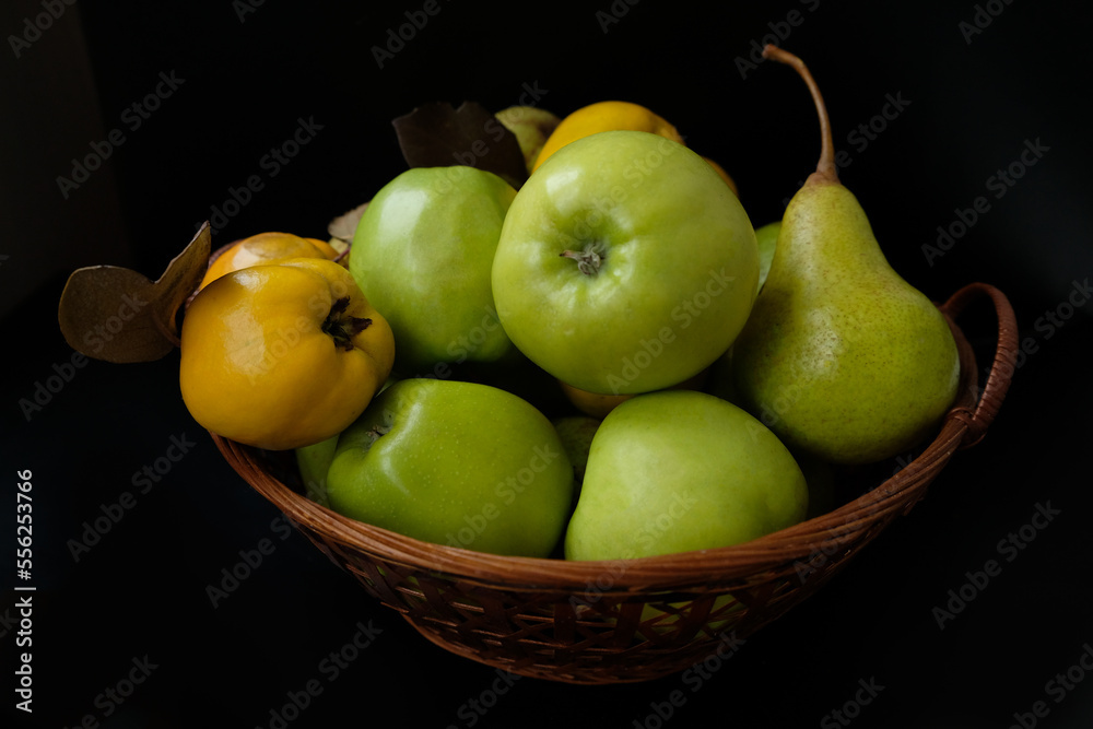 still life of apples, pears and quince in a basket on a black background