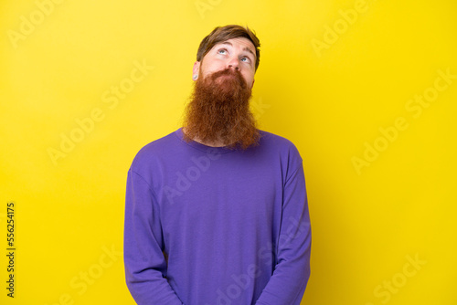 Redhead man with beard isolated on yellow background and looking up