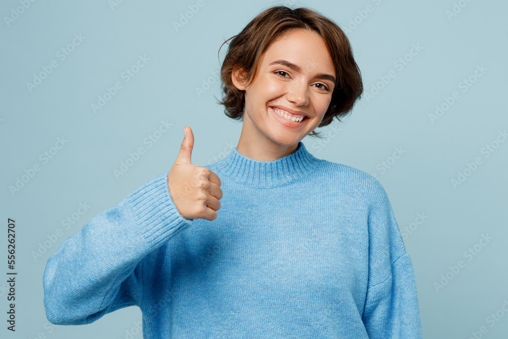Young satisfied happy fun caucasian woman wear knitted sweater look camera showing thumb up like gesture isolated on plain pastel light blue cyan background studio portrait. People lifestyle concept. Young satisfied happy fun caucasian woman wear knitted sweater look camera showing thumb up like gesture isolated on plain pastel light blue cyan background studio portrait. People lifestyle concept.
